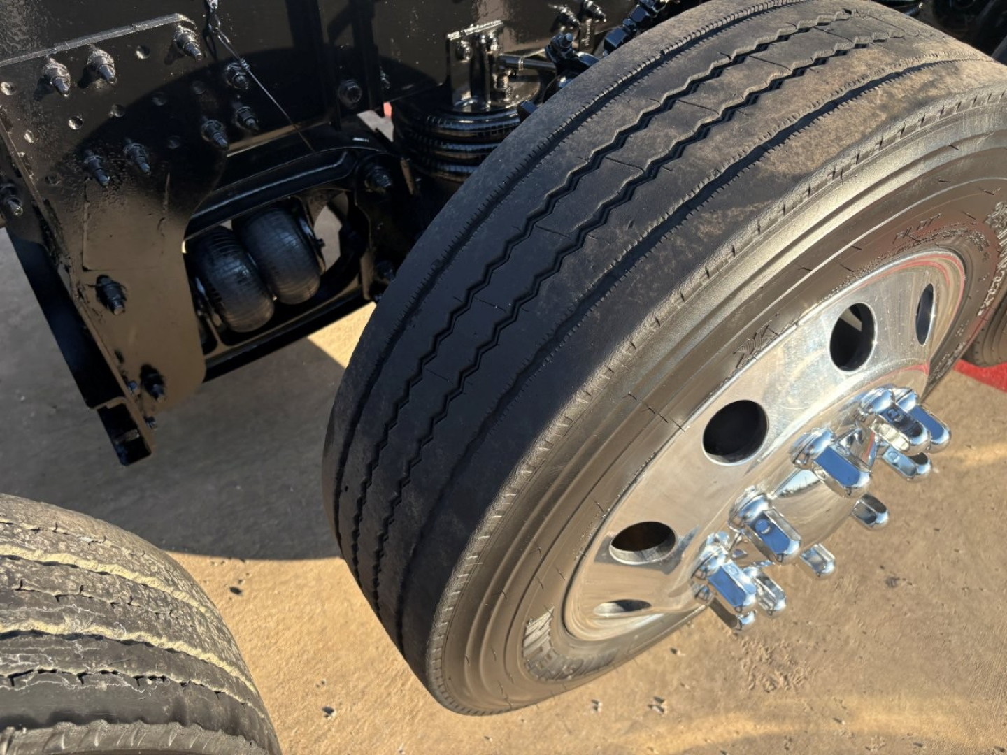 Volvo truck wheel and dual axle area showing front wheel, tire treads, and stainless lug nut covers.