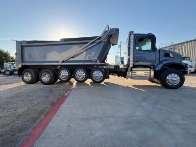 Dump truck with multiple rear axles and a raised dump bed. Side view shows gray cab and gray dump body, chrome wheels, and branding not legible.