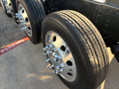 Truck front axle with a dual rear dual wheel setup, chrome lug nuts, and treaded tire visible on a Volvo dump truck chassis.