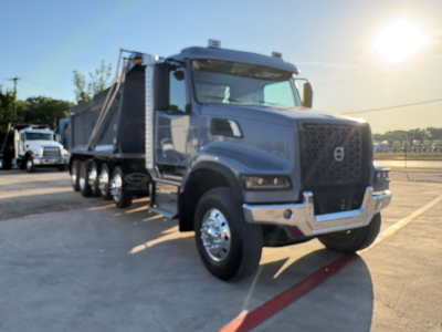 Volvo VHD dump truck oriented front-left view with gray cab and chrome bumper, dual rear axles, dump bed, daytime outdoor lot.