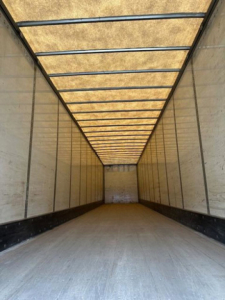 Trailer interior showing long empty van trailer with wooden roof strips and metal side walls.