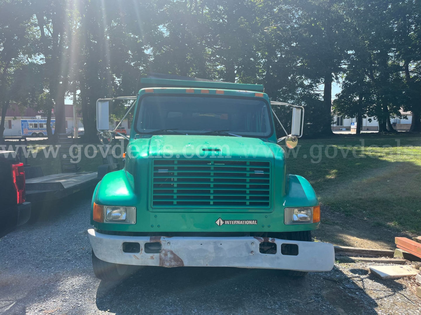 Front view of a green 2002 International 4700 dump truck showing grille, headlights, bumper, and side mirrors.