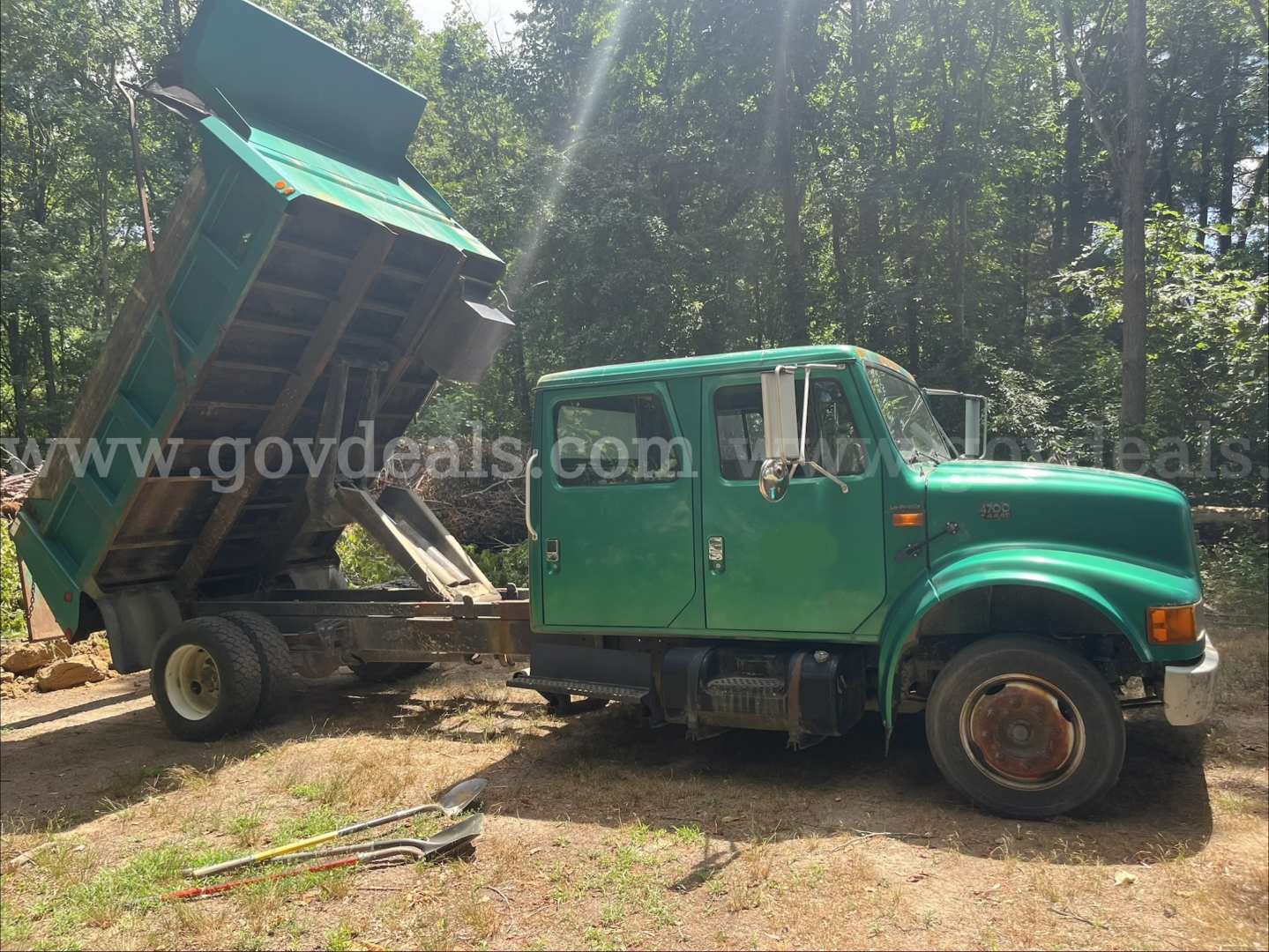 Dump truck with green International 4700 cab and a raised green dump bed, side view showing front wheel and hydraulic mechanism, VIN 1HTSLABMX2H543529.