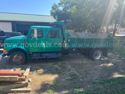 International 4700 dump truck side view showing green cab and dump bed with worn tires and gravel yard.