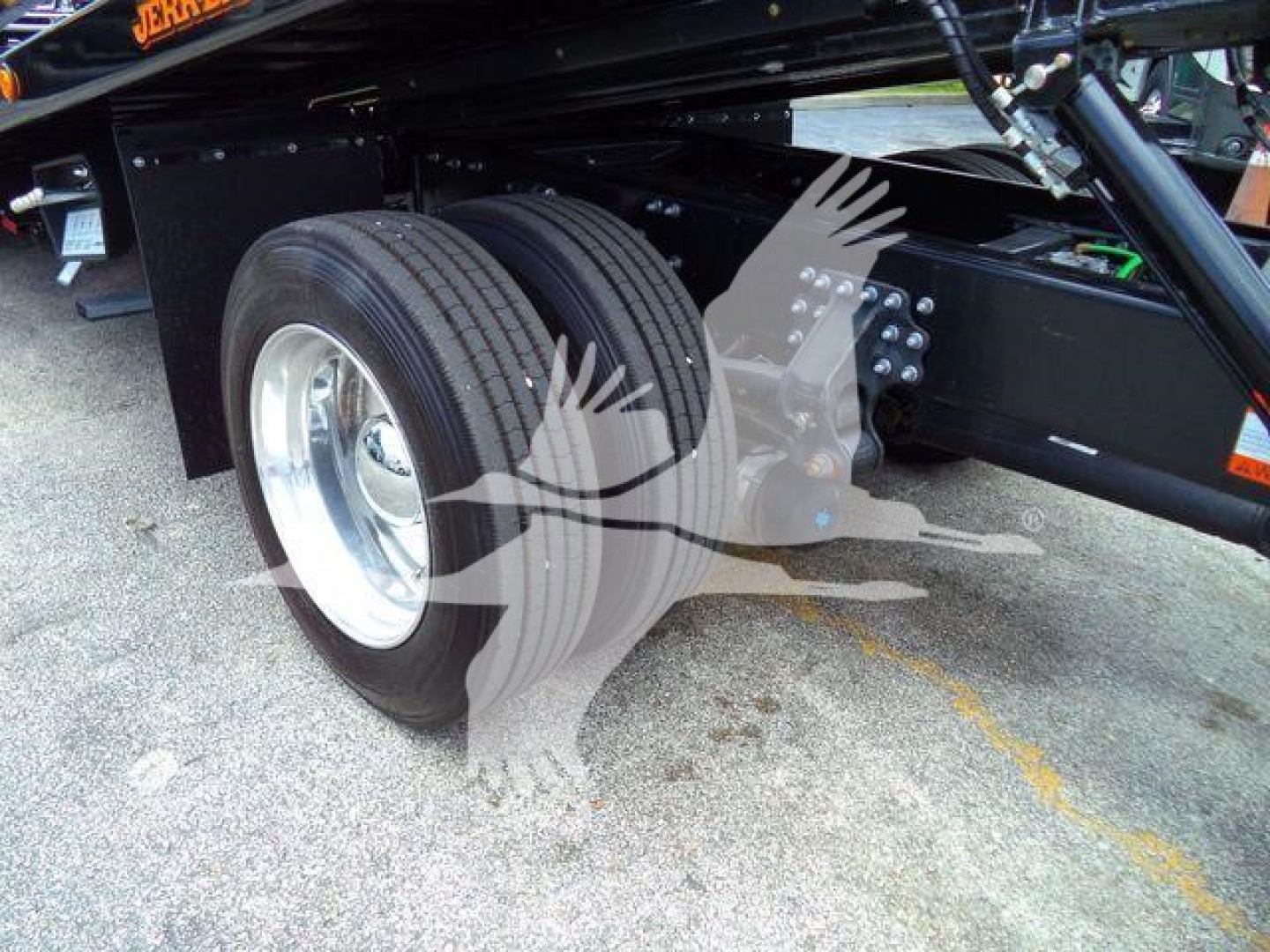 Tractor trailer rear dual tires visible under a Mack MD6 rollback chassis with suspension and frame components.