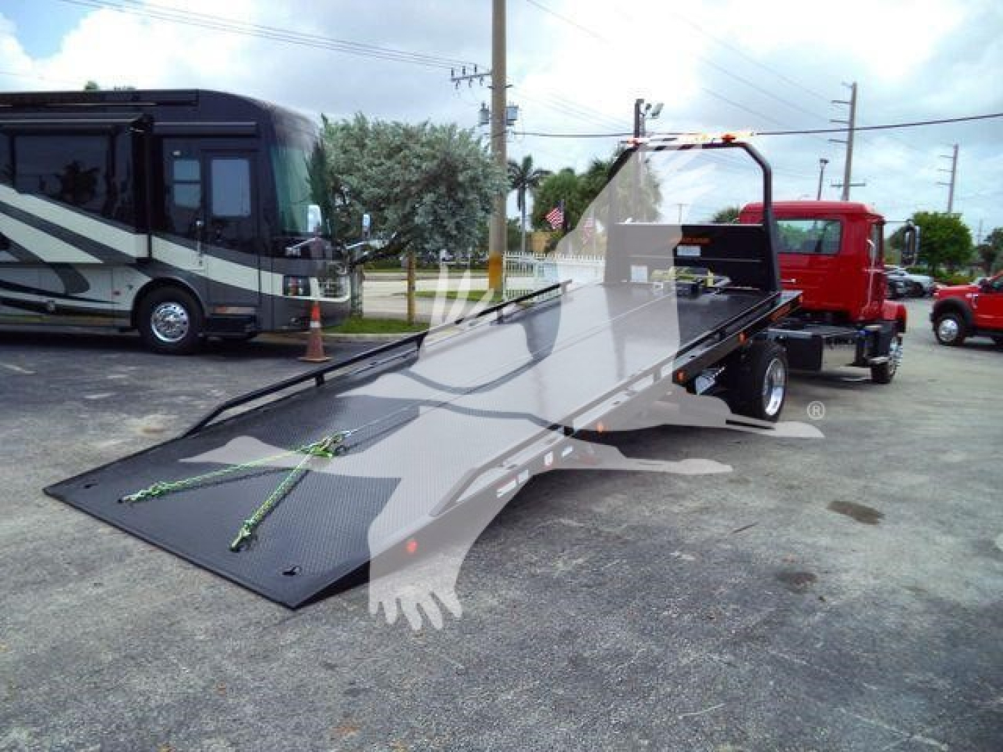 Flatbed tow truck with ramp extended, side view showing 2026 Mack MD6 in a dealership lot.