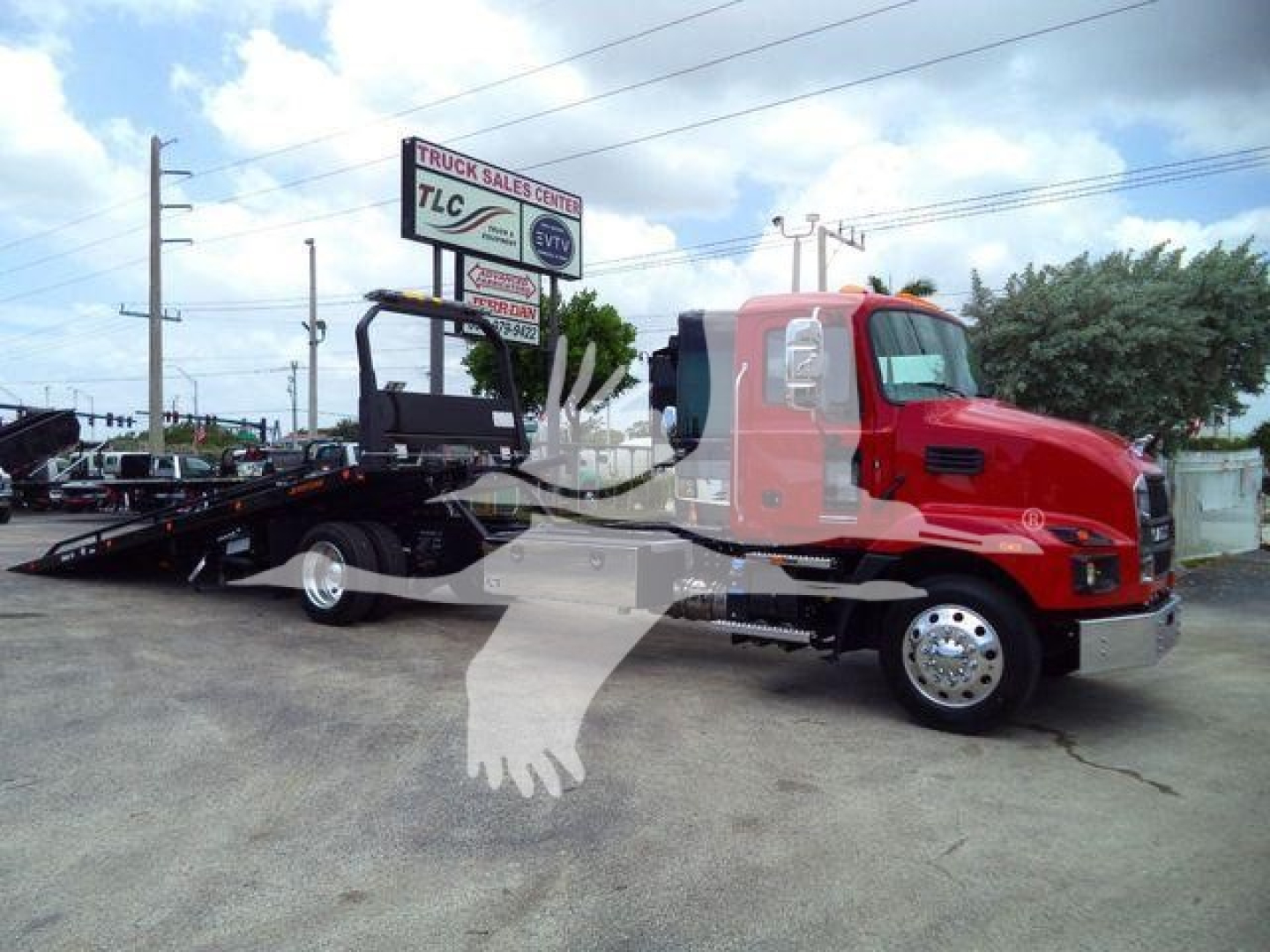 New 2026 Mack MD6 rollback truck in red with black flatbed, side view showing cab and wheel, dealership lot in background.