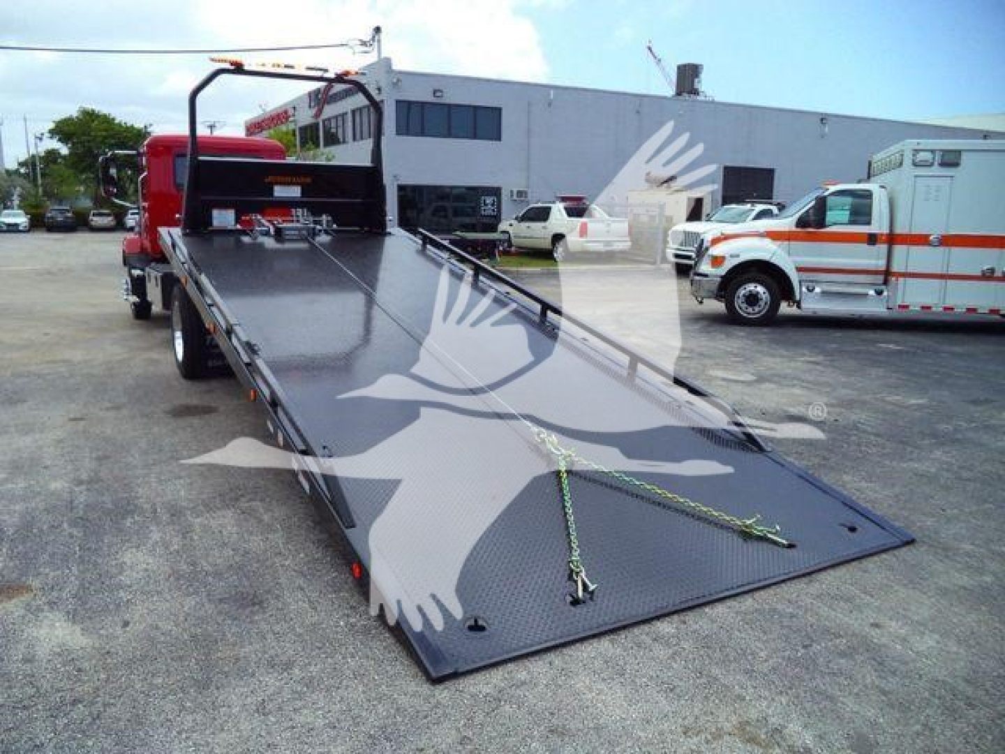 Mack MD6 rollback truck flatbed w/ extended loading ramp and rear wheel-lift area, in a dealership lot.