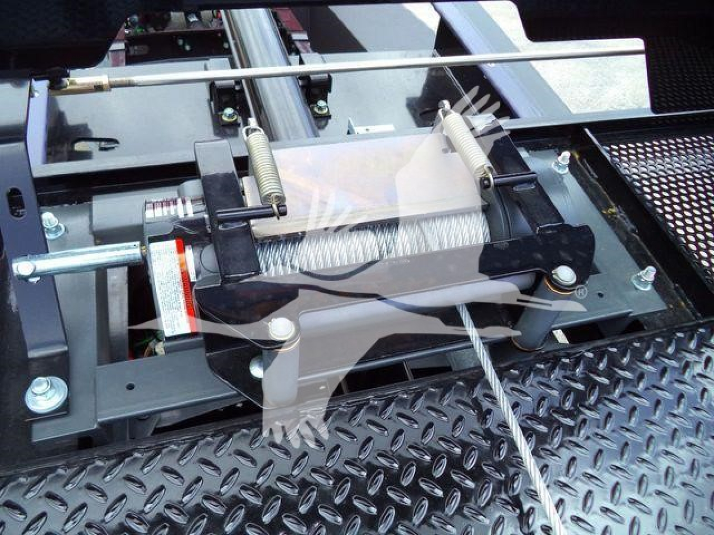 Truck rollback equipment with a spring-loaded winch mechanism and metal Diamond plate surface in view.