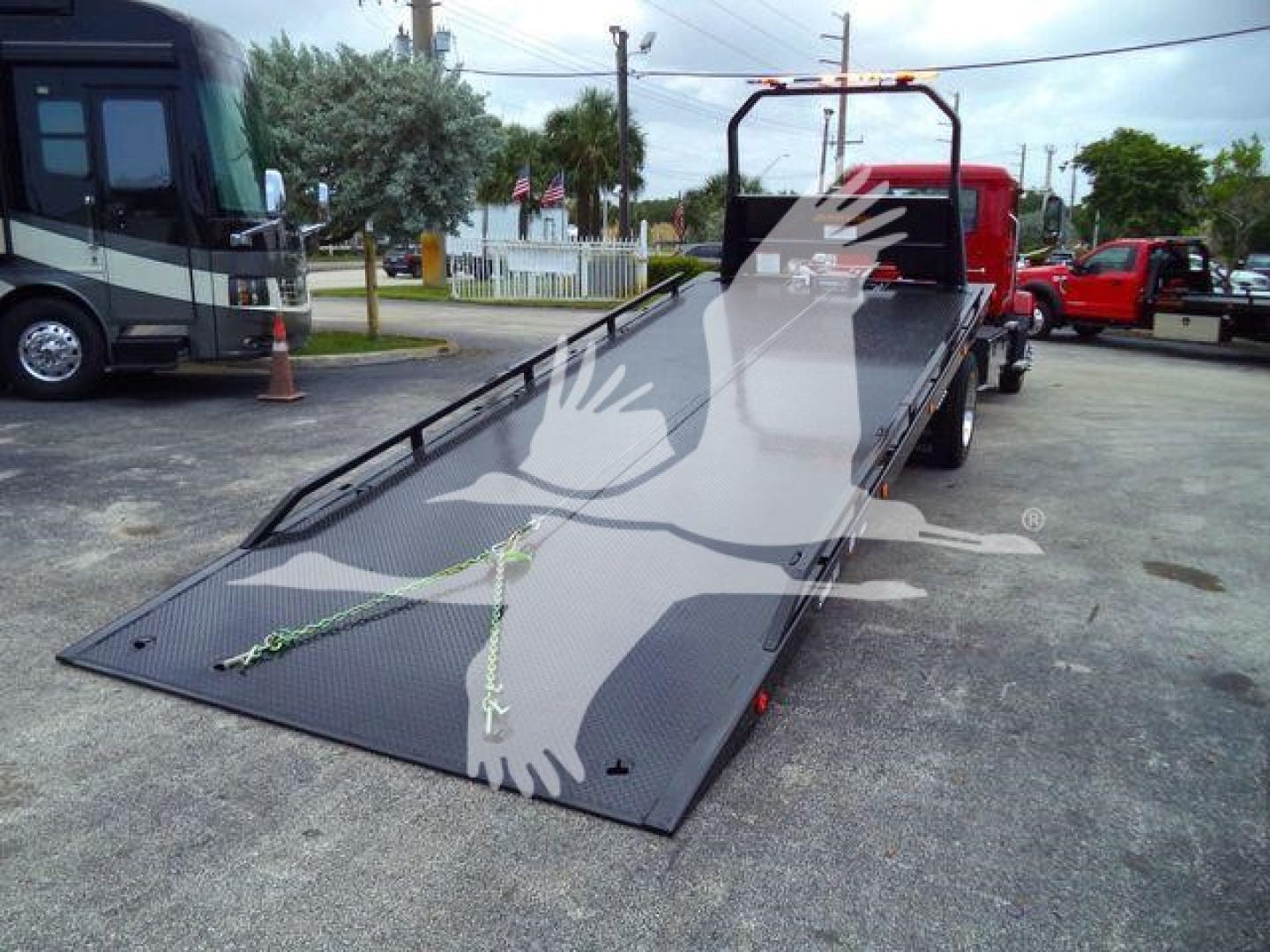 Mack MD6 rollback truck bed with a black flatbed ramp in lowered position and red cab in background.
