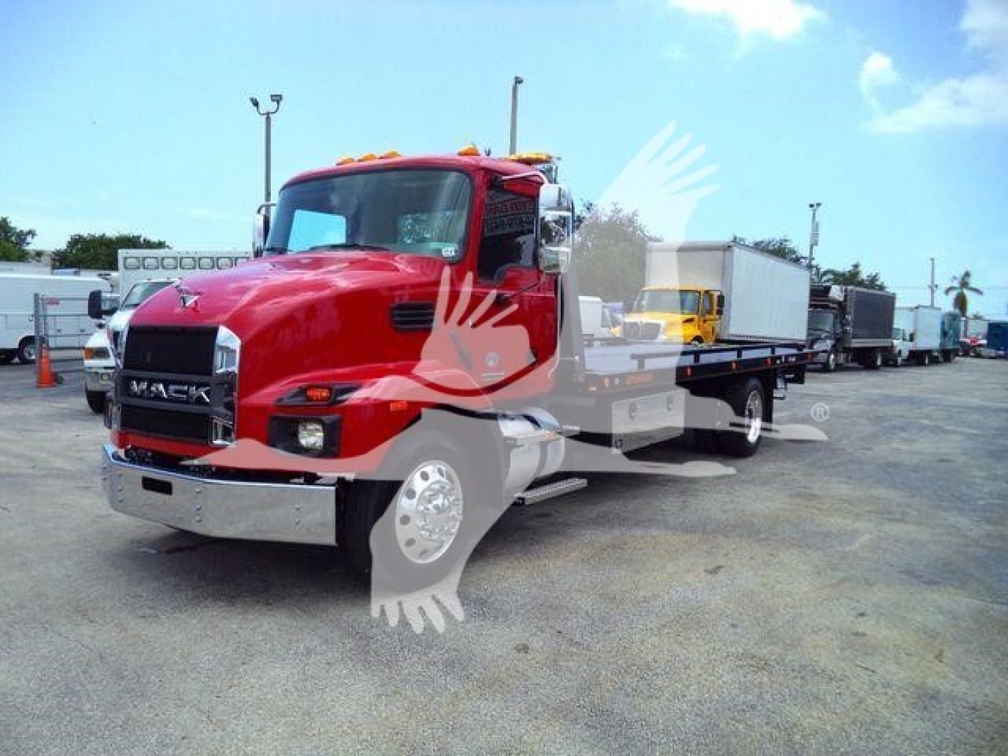 Mack MD6 rollback truck in red showing front and side view with branding, chrome bumper, and nearby trucks in a dealership lot.