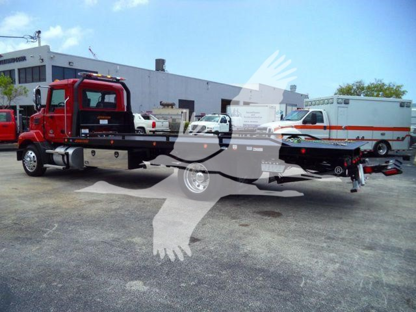Side view of a red Mack MD6 rollback tow truck with a flatbed, parked in lot; faint watermark overlays; no legible model badges visible.