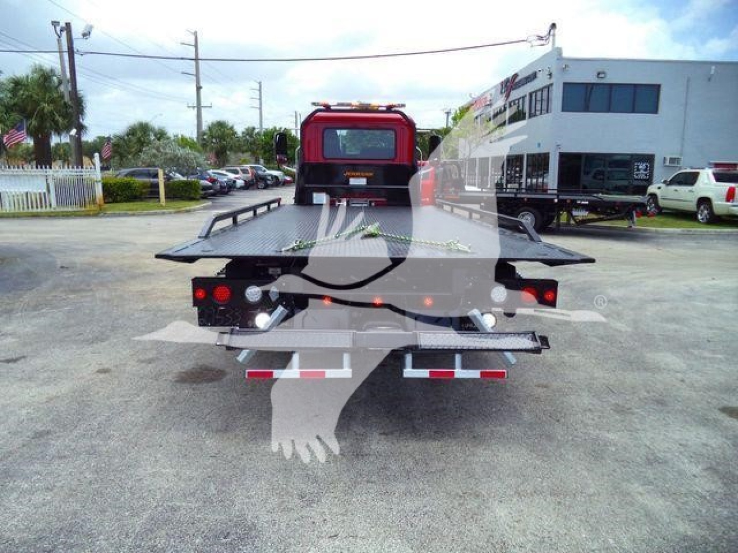 Rear view of a 2026 Mack MD6 rollback/wrecker truck with a flatbed, tailgate, and red cab visible in a dealership lot. Serial/stock visible but not legible.