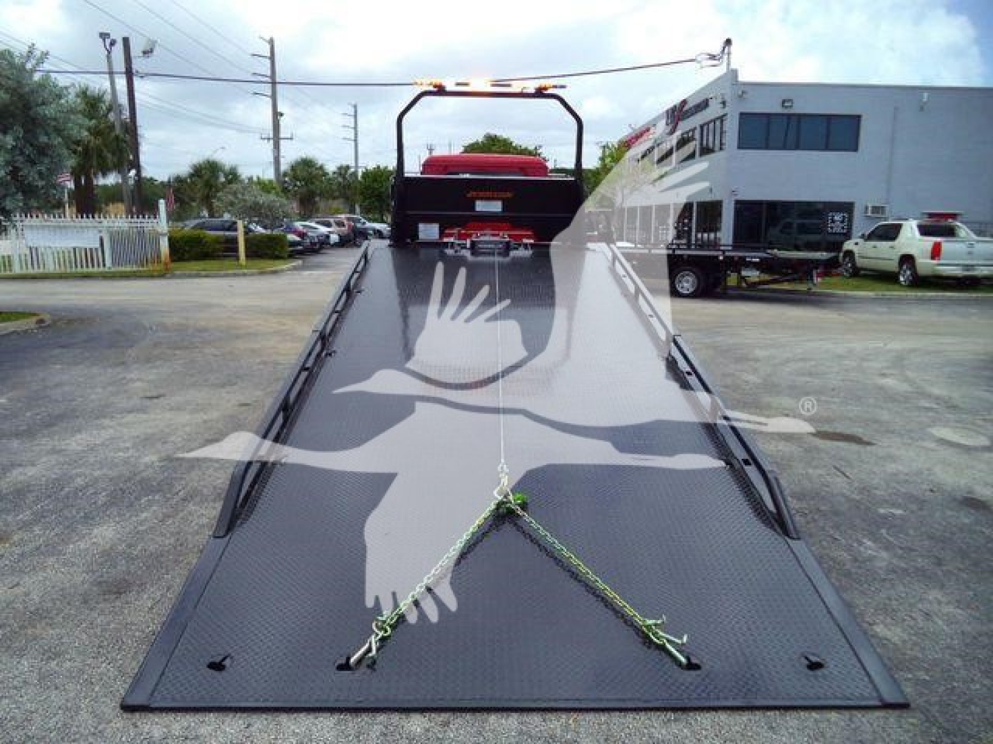 Mack MD6 rollback truck bed showing steel rails and ramp with warning chains and rear cab in distance.