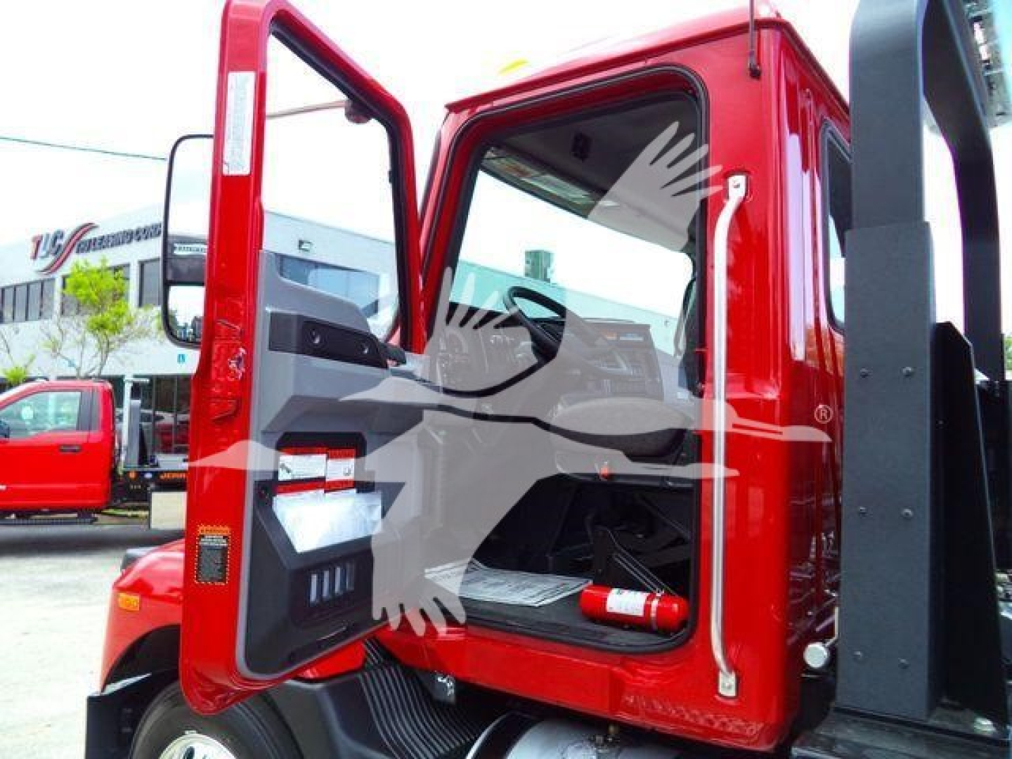 Truck cab door open showing interior of a red Mack MD6 rollback truck with side mirror and steps.