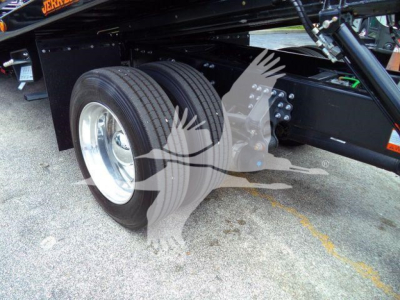 Tractor trailer rear dual tires visible under a Mack MD6 rollback chassis with suspension and frame components.