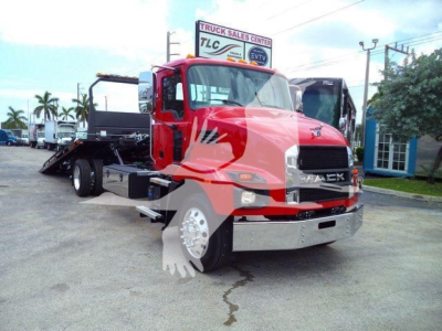 Front-left view of a red 2026 Mack MD6 tow truck with large chrome bumper and grille, rollback bed visible at rear, dealership lot in background.