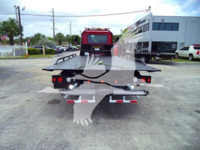 Rear view of a 2026 Mack MD6 rollback/wrecker truck with a flatbed, tailgate, and red cab visible in a dealership lot. Serial/stock visible but not legible.
