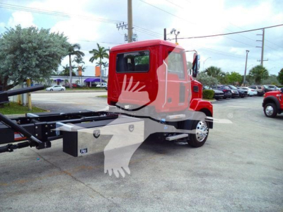 Tractor unit cab of a red Mack MD6 roll-back truck showing chassis and wheel hub; visible chain and frame behind cab with equipment box.