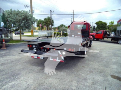 Rear view of a red Mack MD6 rollback truck showing a flatbed and towing equipment. Visible text includes stock banner and rear lights; no legible model serials.