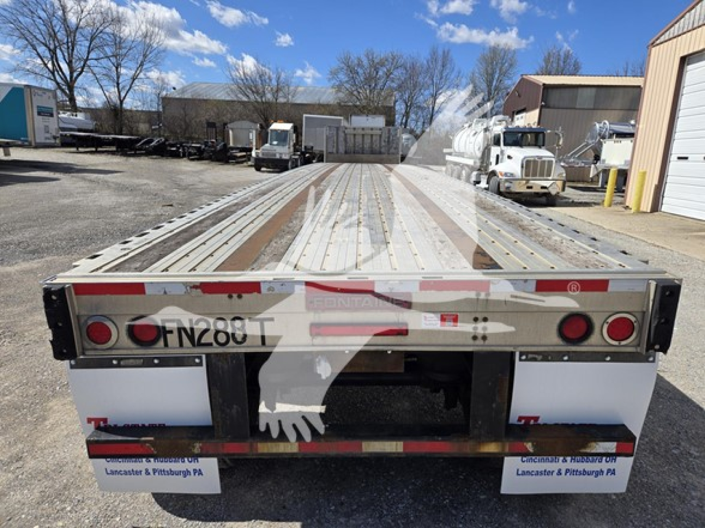 Trailer rear view showing flatbed deck and taillights on Fontaine Infinity trailer, back plate with license and mud flaps.
