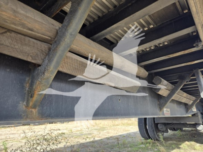 Flatbed trailer undercarriage showing steel rails, support beams, and wheel hub.
