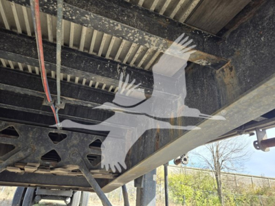 Trailer frame undercarriage with metal beams, wiring, and support structure visible; light and shadows show underside of Fontaine Infinity flatbed trailer.