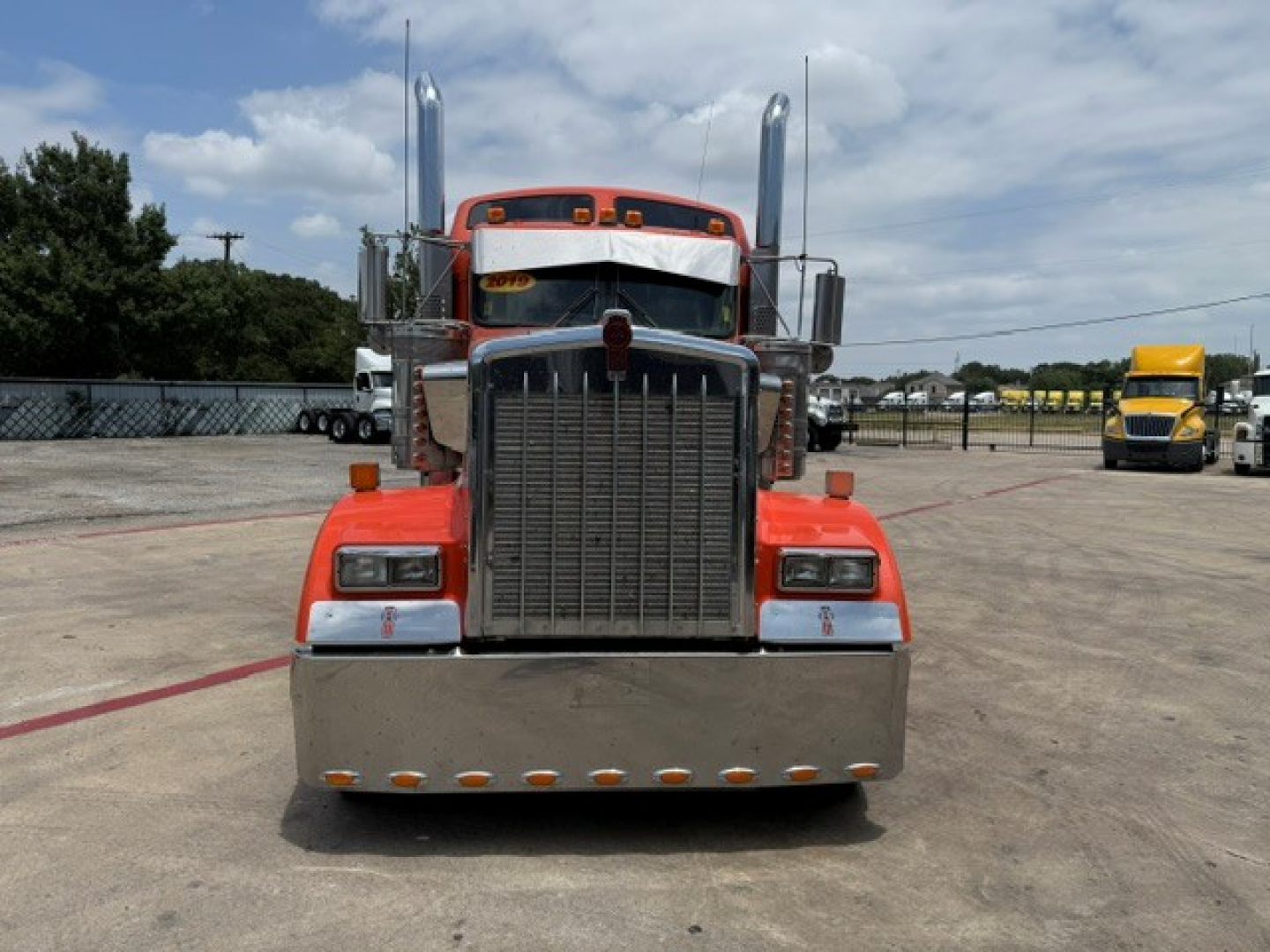 Kenworth W900 front view showing large grille, chrome bumper, dual tall exhaust stacks, rectangular headlights, orange cab paint.