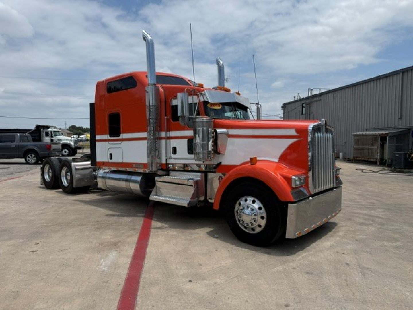 Kenworth W900 semi-truck in orange and white color, cab view with chrome exhaust stacks and large front grille.