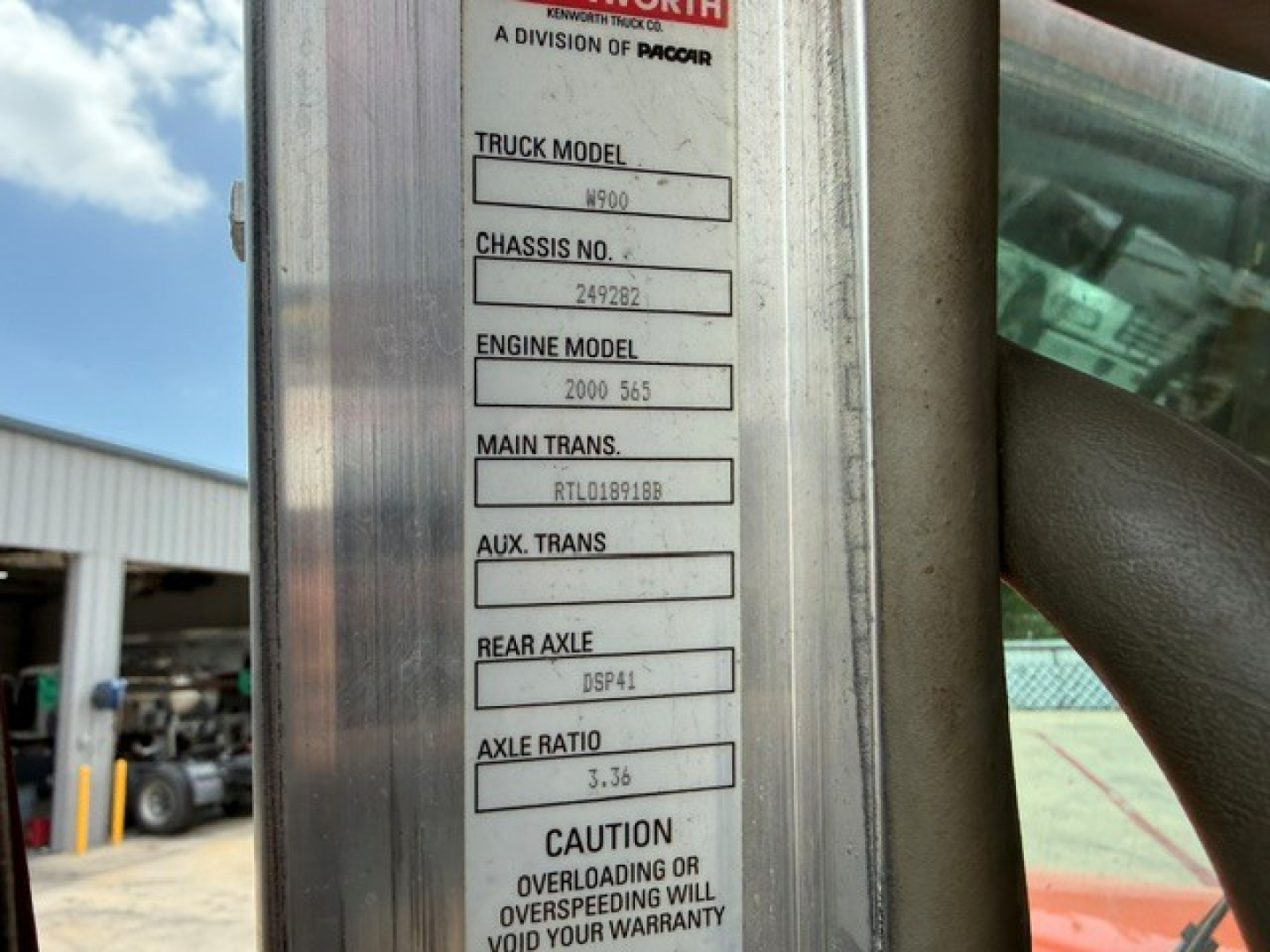Truck model information plate on Kenworth W900 showing TRUCK MODEL W900, CHASSIS NO. 249282, ENGINE MODEL 2000 545, MAIN TRANS. RTL089188, REAR AXLE DSP41, AXLE RATIO 3.36, CAUTION label.