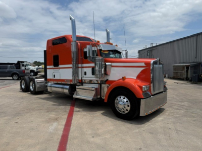 Kenworth W900 semi-truck in orange and white color, cab view with chrome exhaust stacks and large front grille.