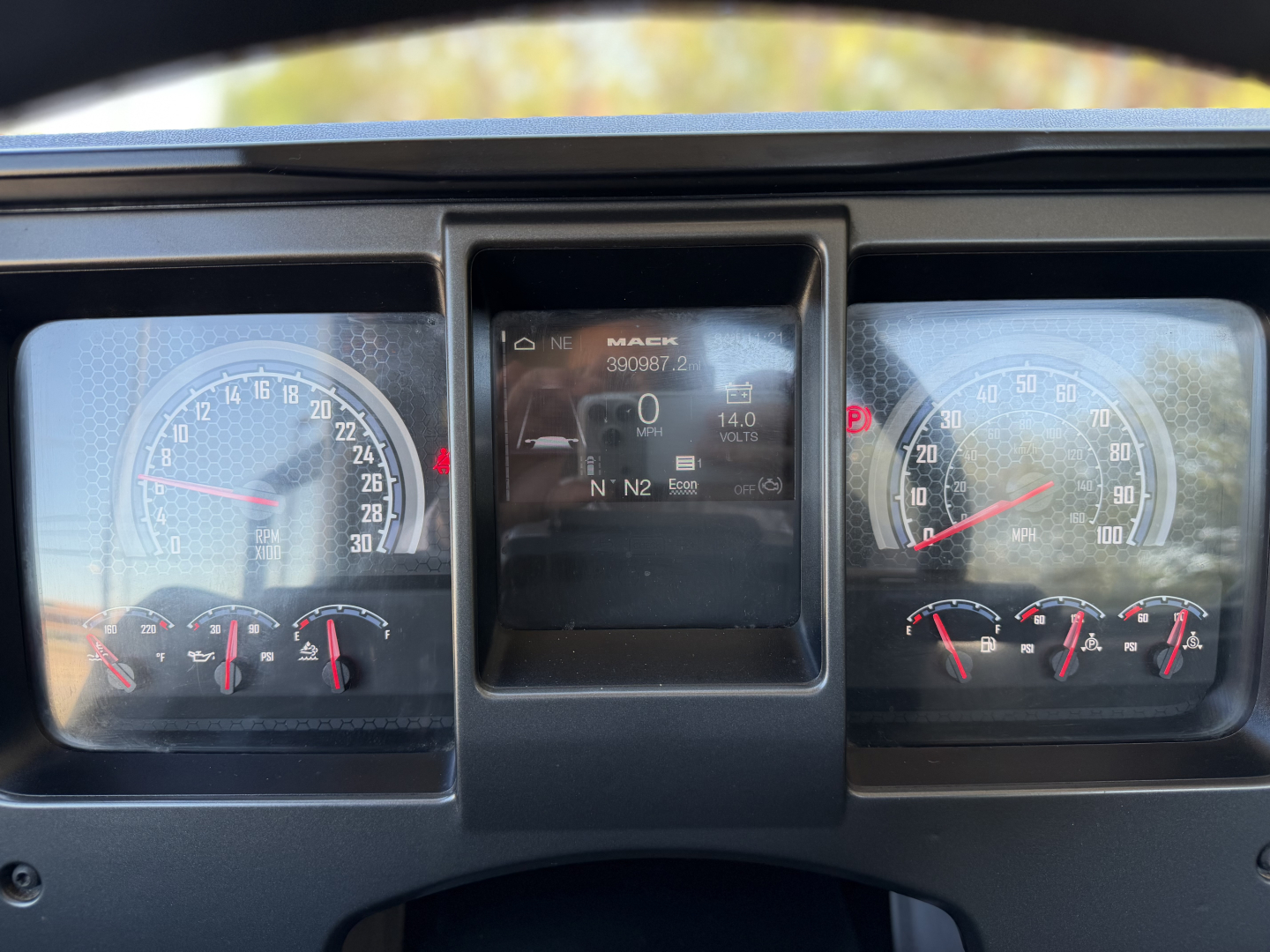 Dashboard view of a 2023 Mack ANTHEM 64T showing instrument gauges and central digital display. Center screen shows Mack logo and odometer; left and right gauges show speedometer and RPM scales.