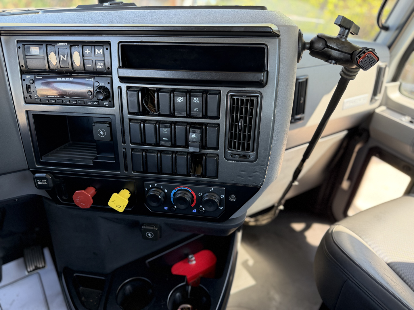 Dashboard of a 2023 Mack Anthem 64T truck cab showing radio, climate controls, auxiliary switches, steering wheel stalk, and driver seat. Visible labels and controls in center console.