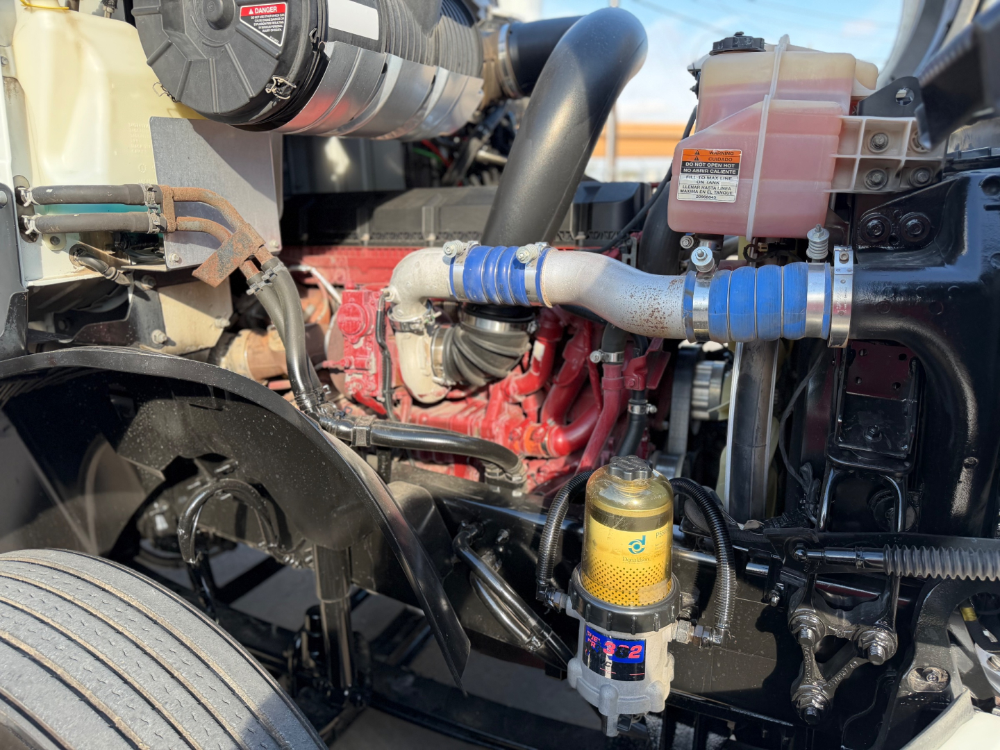 Mack ANTHEM 64T engine bay view showing coolant hoses, yellow oil filter, and fuel/wear components with red engine block.