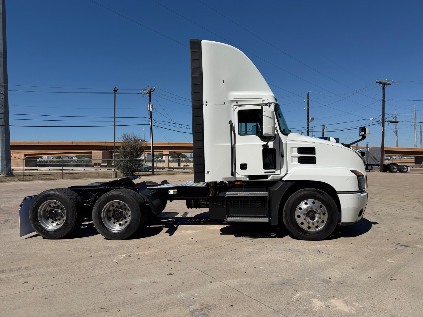 Truck side view of a white 2023 Mack ANTHEM 64T conventional daycab showing cab interior steps and dual rear axles.