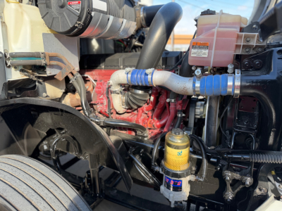 Mack ANTHEM 64T engine bay view showing coolant hoses, yellow oil filter, and fuel/wear components with red engine block.