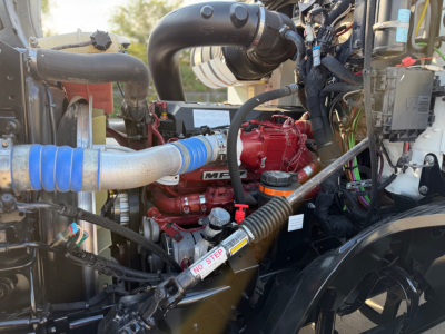 Mack ANTHEM 64T engine bay showing red engine block, blue hose, black intake, and wiring harness.