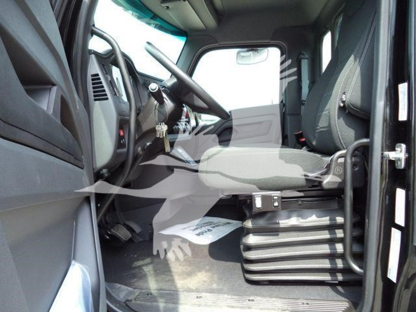 Truck cab interior showing driver's seat, steering wheel, pedals, and floor area of a Kenworth T-series cab. Visible text: none legible.