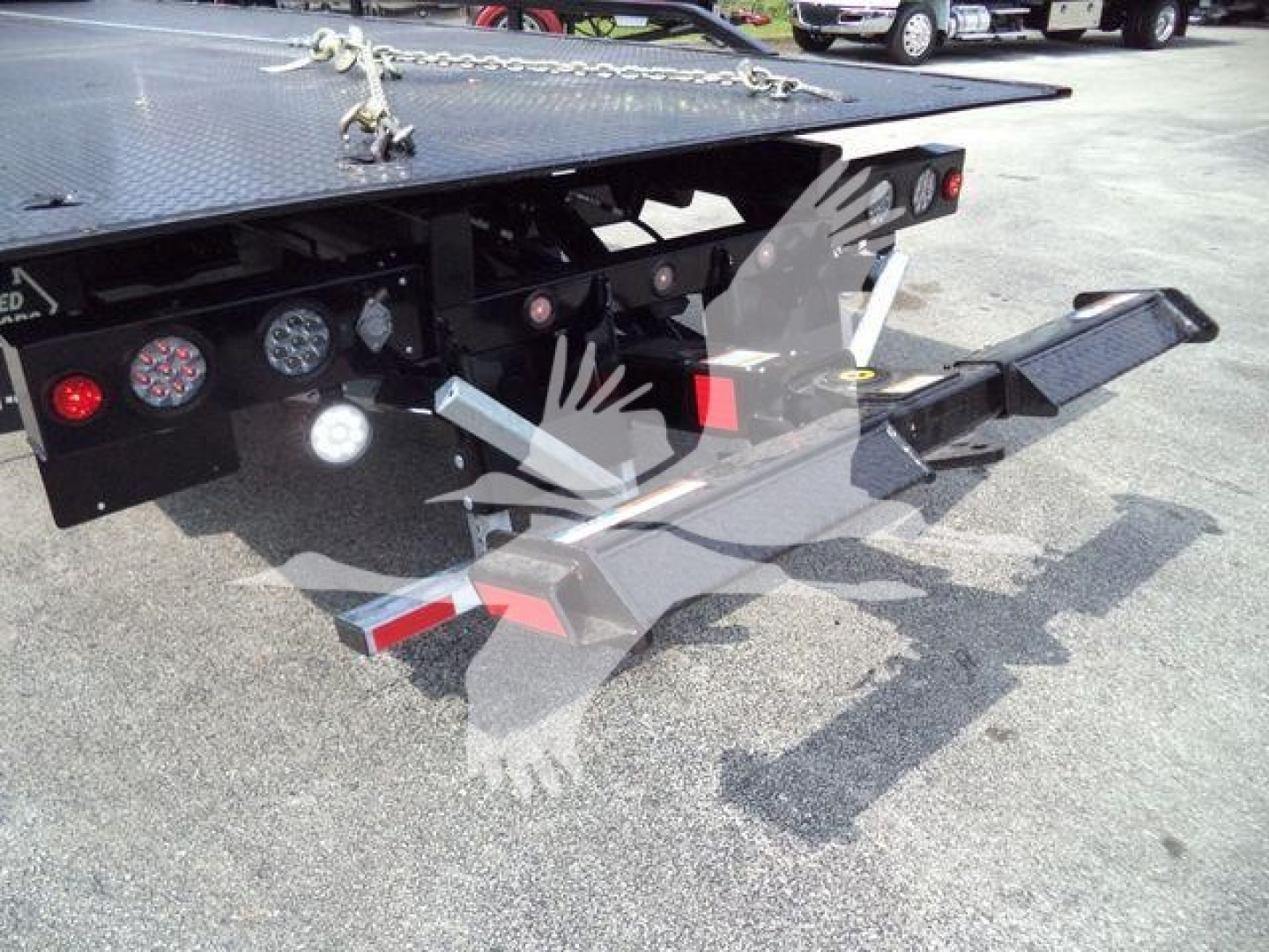 Truck rear with hydraulic rollback hitch and loading platform showing steel surfaces and lights.