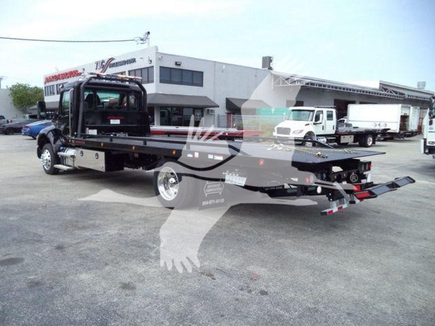 Kenworth T280 rollback tow truck side view showing flatbed with ramps and chassis, dealership lot in background.