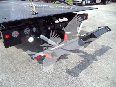 Truck rear with hydraulic rollback hitch and loading platform showing steel surfaces and lights.