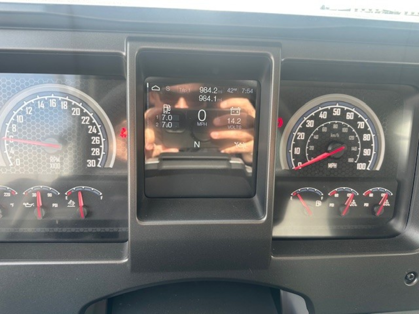 Vehicle dashboard of a 2026 Mack GR64F showing gauge cluster and central digital display with steering wheel reflection.