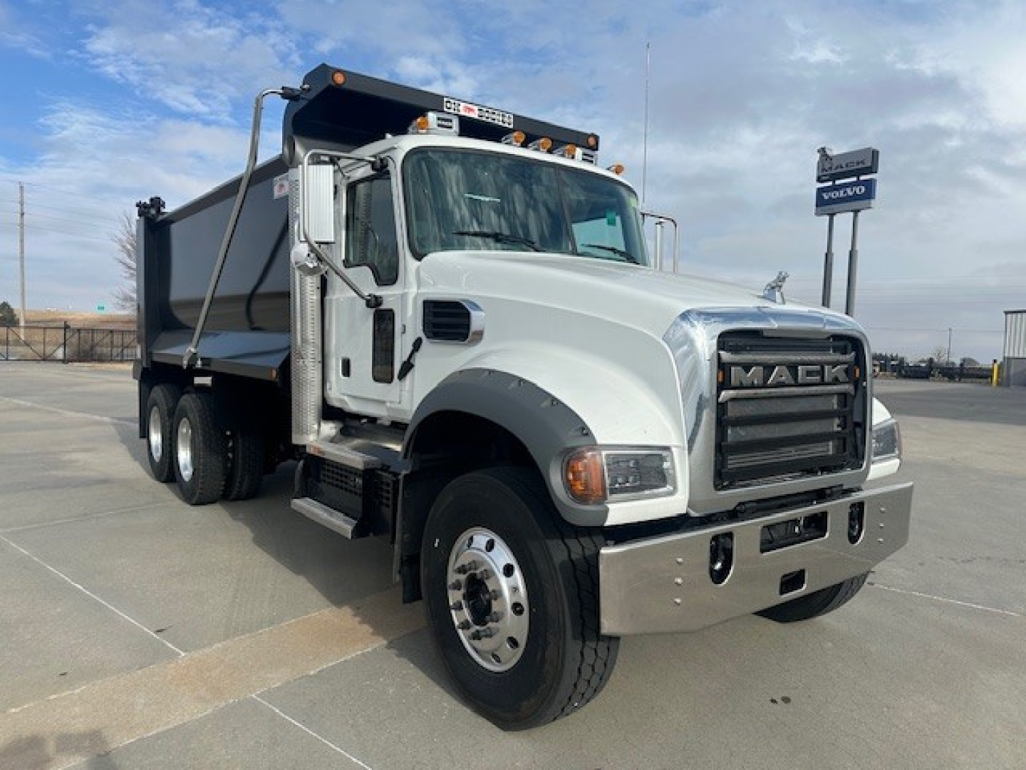 Mack GR64F dump truck in white/gray, front three-quarter view, showing cab, grille with MACK letters, side mirrors, and dump bed.