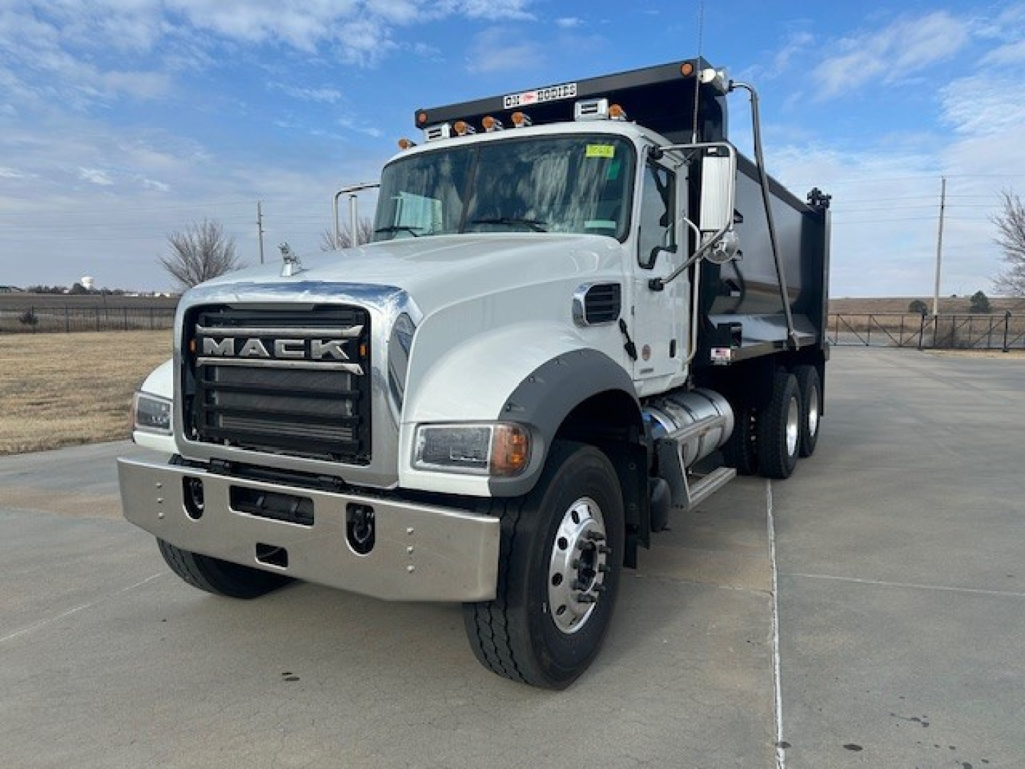 Mack GR64F dump truck in white chassis in-service view showing front grille with 'MACK' emblem and dump bed.