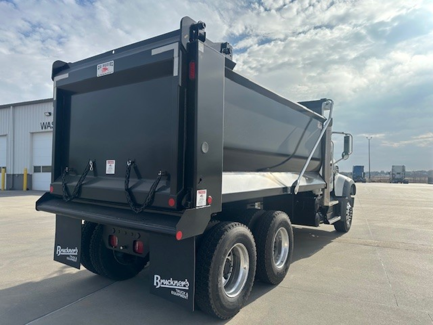 Dump truck rear and side view showing dump bed and Mack GR64F chassis with six-wheeled rear axle configuration.