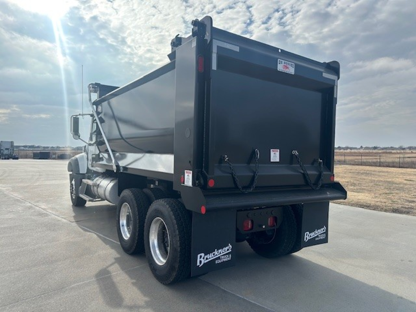 Dump truck rear view showing Mack GR64F dump bed and dual rear axles with mud flaps and tailgate latch details.