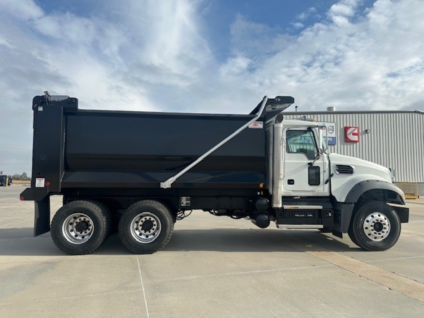 Dump truck side view showing 2026 Mack GR64F dump truck with black dump bed and white cab, six-wheel configuration.