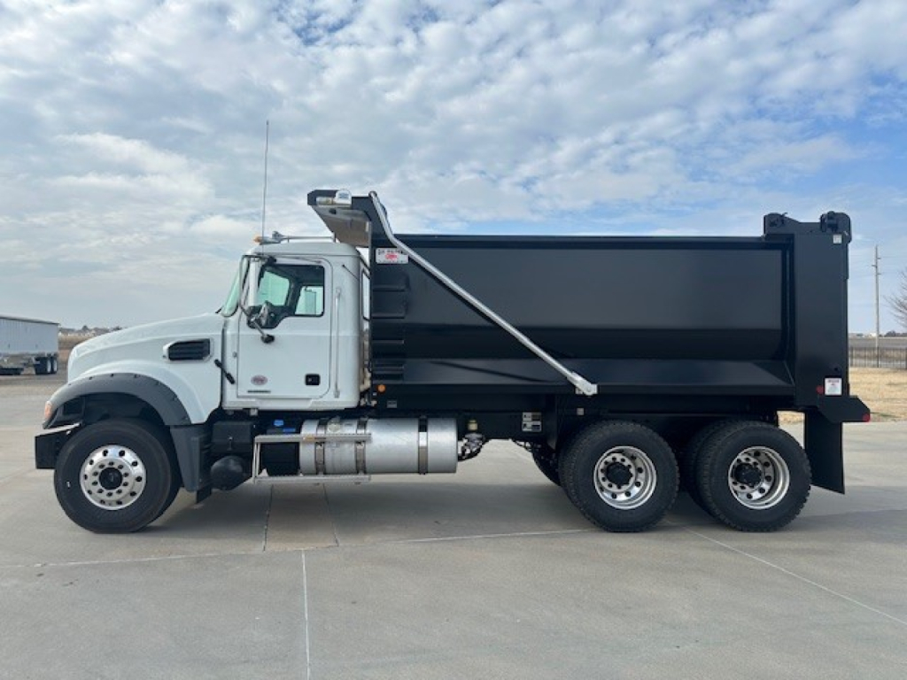 Mack GR64F dump truck side view showing black dump bed, white cab, dual rear axles and fuel tanks.