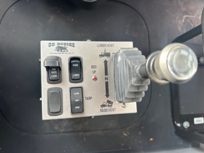 DS BODIES control module showing lower hoist with toggle levers labeled TAL GATE LOCK, RAISE, LOWER, TARP, OPEN, CLOSE; gauge with gear-like lever on right; arrows indicating bed up/down and raise hoist.