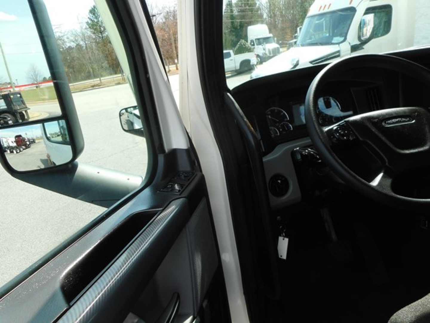 Truck interior view from driver side door showing dashboard steering wheel and side mirror.
